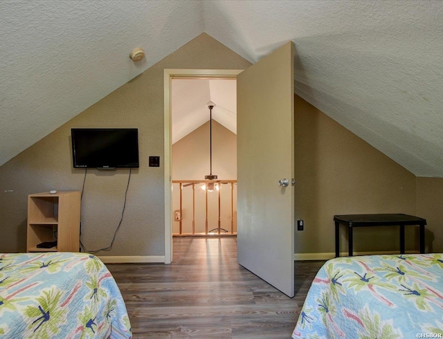 bedroom featuring vaulted ceiling, a textured ceiling, baseboards, and wood finished floors