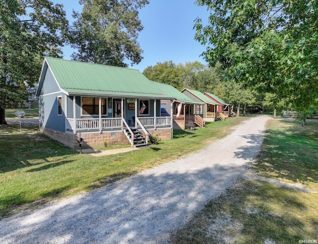 view of front of property with metal roof, driveway, a porch, and a front lawn