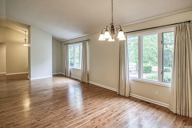 spare room featuring a notable chandelier, a textured ceiling, wood finished floors, lofted ceiling, and visible vents