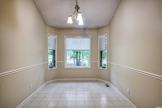 spare room with an inviting chandelier, light tile patterned floors, baseboards, and a textured ceiling