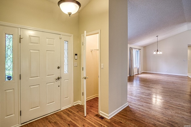 entrance foyer with an inviting chandelier, a textured ceiling, dark wood-type flooring, and lofted ceiling