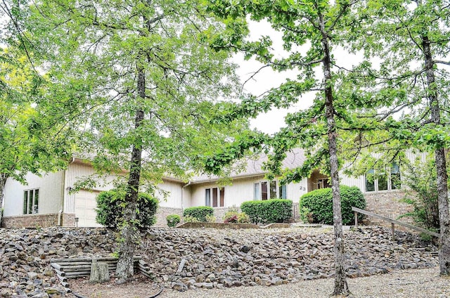 view of property hidden behind natural elements featuring brick siding and an attached garage