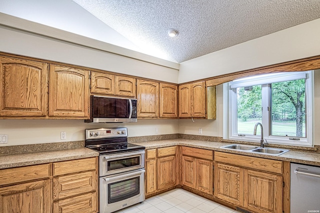 kitchen with a sink, a textured ceiling, brown cabinetry, stainless steel appliances, and lofted ceiling