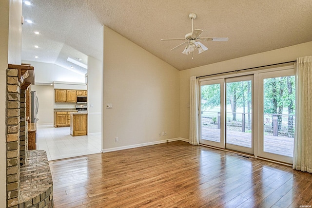 empty room with a textured ceiling, light wood finished floors, ceiling fan, and vaulted ceiling