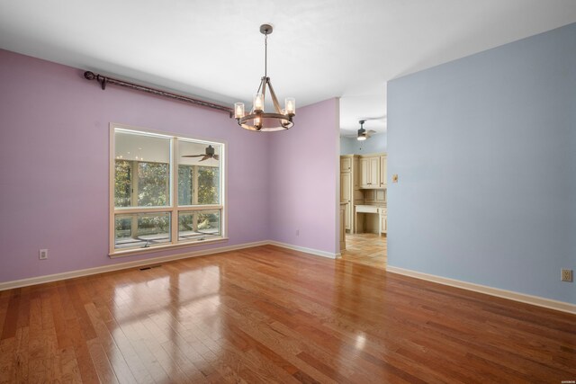 empty room featuring wood-type flooring, baseboards, and ceiling fan with notable chandelier