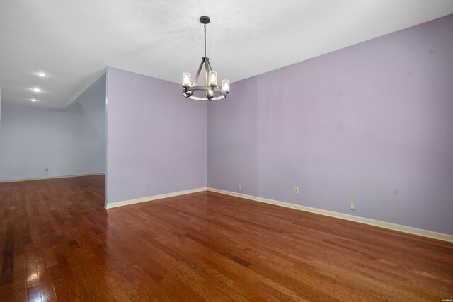 spare room with a notable chandelier, hardwood / wood-style flooring, and baseboards