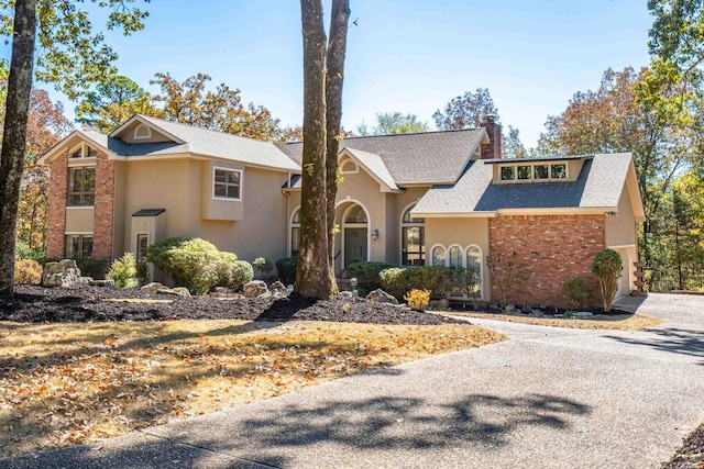 view of front of property with a shingled roof, driveway, a chimney, and stucco siding