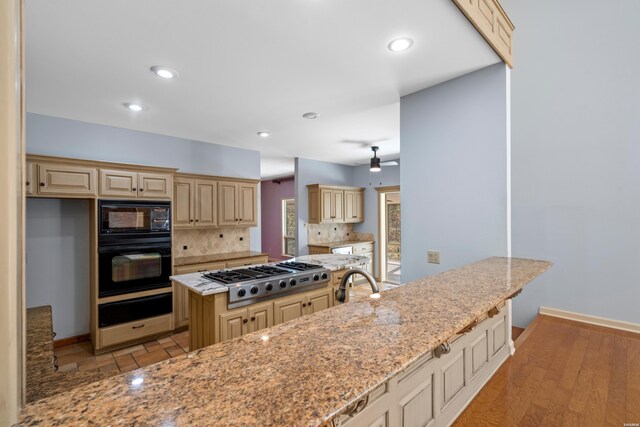 kitchen featuring light stone countertops, black appliances, backsplash, and cream cabinetry