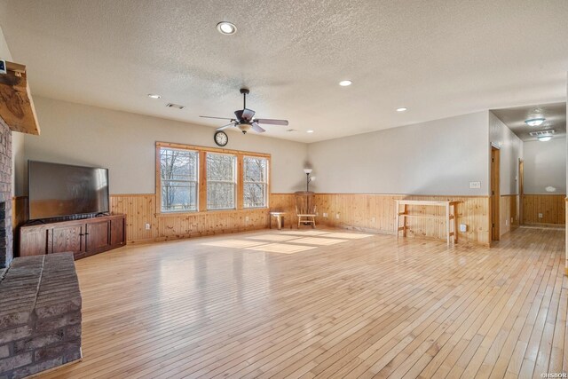 living area with visible vents, a ceiling fan, a wainscoted wall, a textured ceiling, and light wood-type flooring