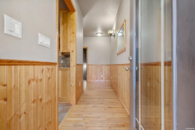 hall featuring a wainscoted wall, a textured ceiling, light wood-type flooring, wood walls, and a sink