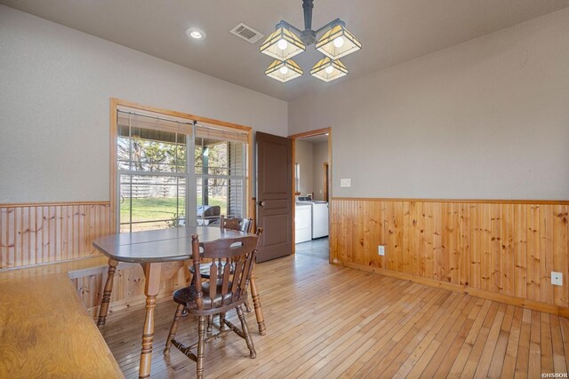 dining area featuring visible vents, light wood-style flooring, wainscoting, wooden walls, and independent washer and dryer