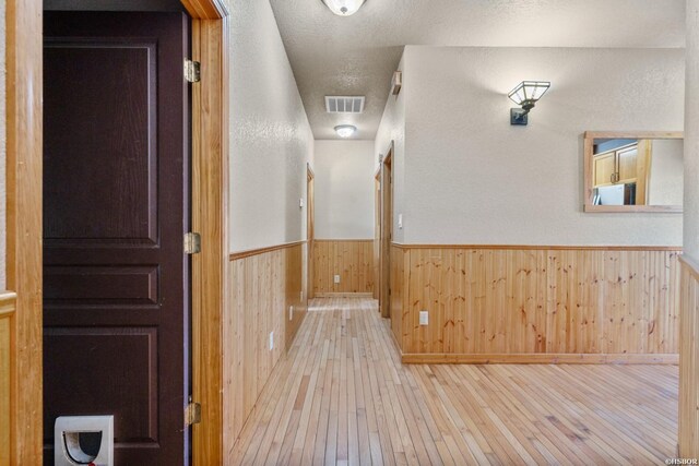 corridor featuring visible vents, light wood-style floors, wainscoting, wooden walls, and a textured ceiling