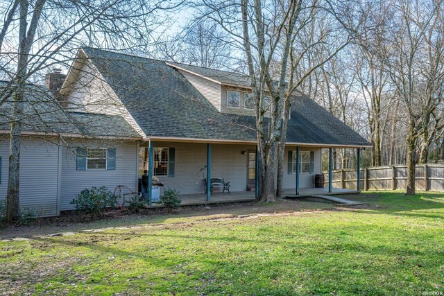 back of property with roof with shingles, a lawn, and fence