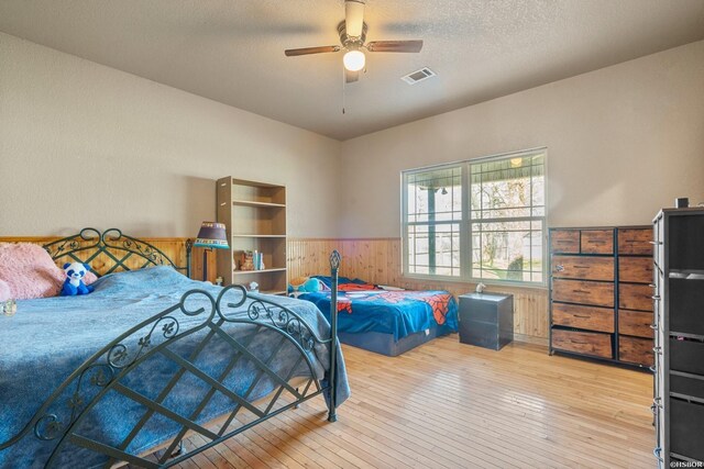 bedroom featuring visible vents, wainscoting, light wood-style flooring, a textured ceiling, and wood walls