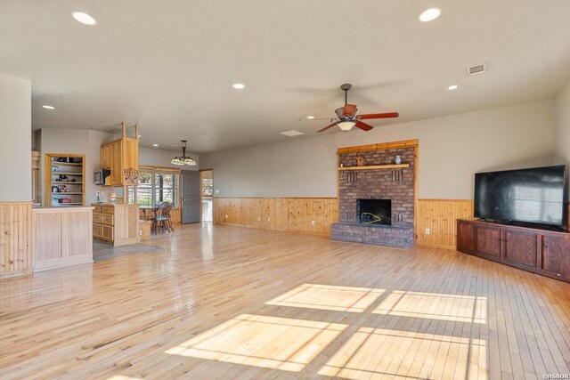 unfurnished living room featuring a wainscoted wall, light wood-type flooring, a fireplace, and visible vents