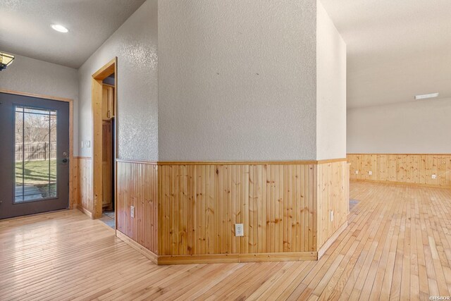 hallway with light wood-type flooring, a wainscoted wall, a textured wall, and wooden walls