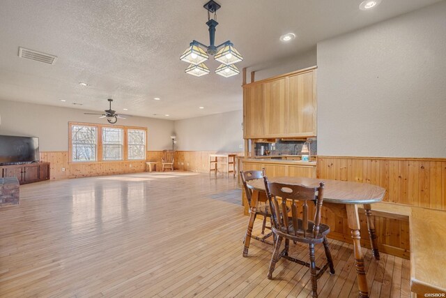 dining room featuring light wood finished floors, visible vents, wainscoting, wood walls, and a textured ceiling