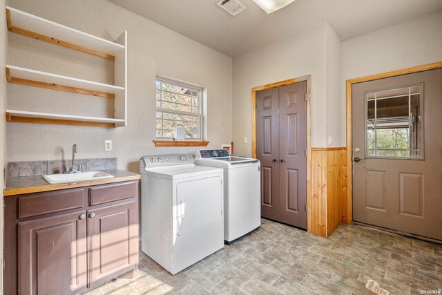 washroom featuring a wainscoted wall, a sink, visible vents, washer and dryer, and cabinet space