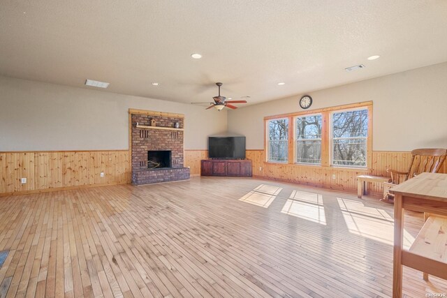 unfurnished living room with a wainscoted wall, a fireplace, visible vents, and light wood-style floors