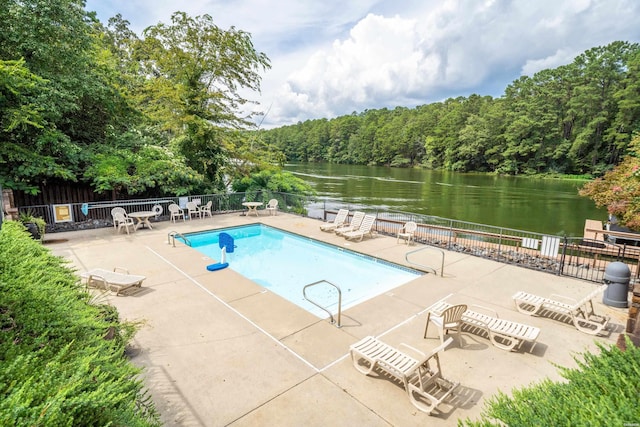 pool featuring a patio area, a wooded view, a water view, and fence