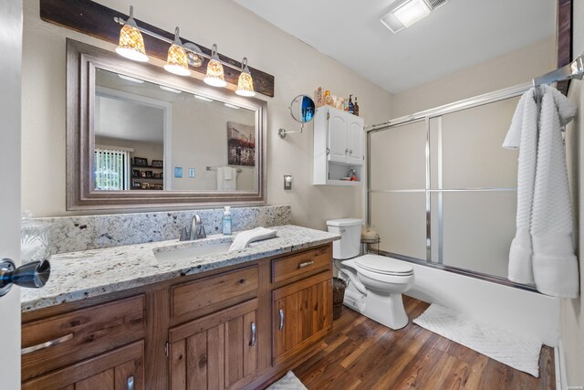 bathroom with visible vents, bath / shower combo with glass door, toilet, wood finished floors, and vanity