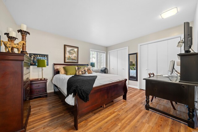 bedroom featuring wood finished floors, baseboards, and two closets