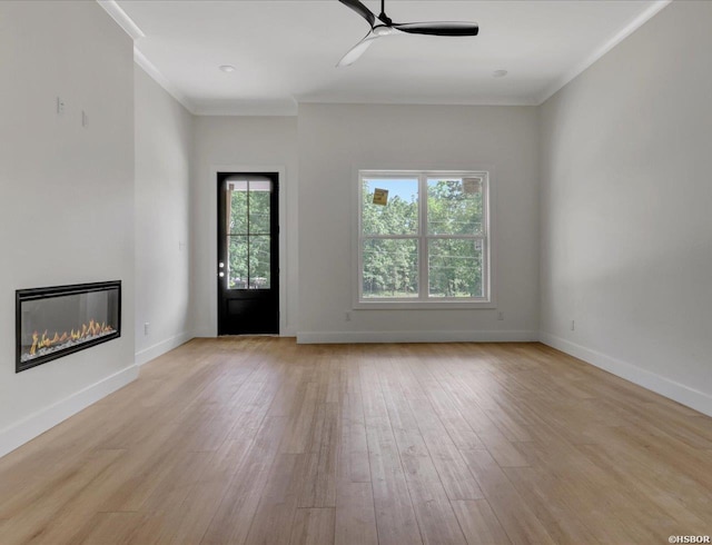 unfurnished living room with ornamental molding, ceiling fan, a glass covered fireplace, light wood-style flooring, and baseboards