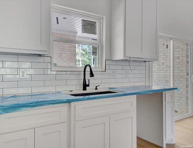 kitchen featuring a sink, decorative backsplash, white cabinetry, light wood-style flooring, and light stone countertops
