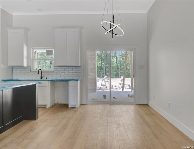 kitchen with light wood finished floors, white cabinets, tasteful backsplash, crown molding, and baseboards