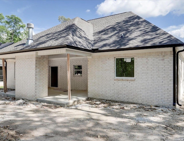 rear view of house with brick siding and roof with shingles