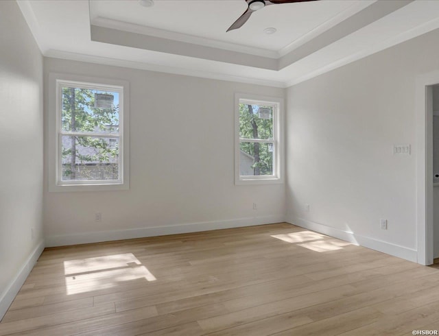 empty room featuring a tray ceiling, light wood finished floors, ornamental molding, ceiling fan, and baseboards