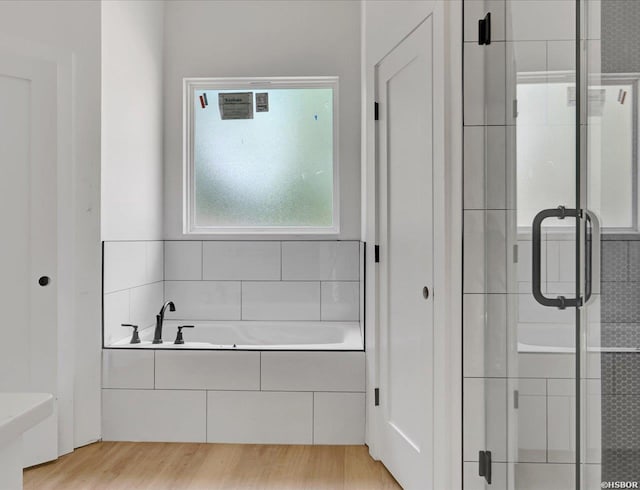bathroom with a stall shower, a bath, and wood finished floors