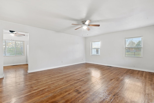 empty room featuring plenty of natural light, ceiling fan, wood-type flooring, and baseboards