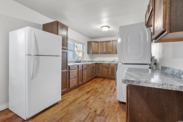 kitchen featuring stacked washer and dryer, brown cabinetry, freestanding refrigerator, light wood-style floors, and a sink