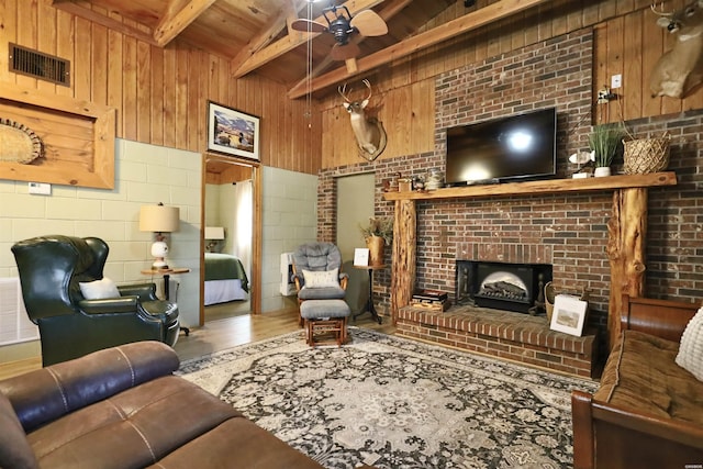 living room featuring beam ceiling, a brick fireplace, visible vents, and wooden walls