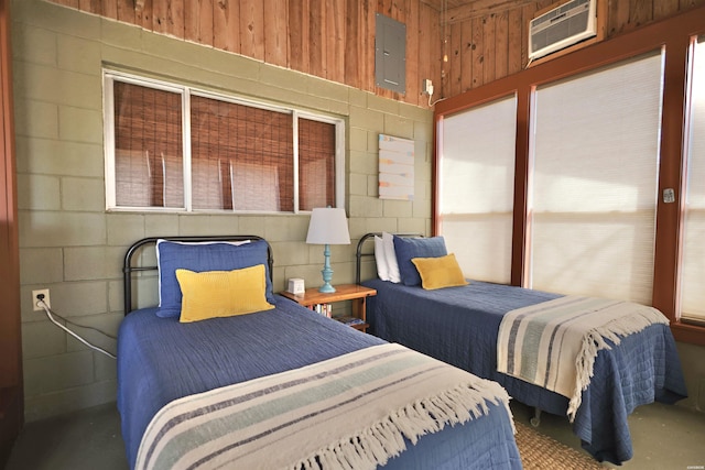 bedroom with concrete flooring, concrete block wall, electric panel, and a wall mounted air conditioner