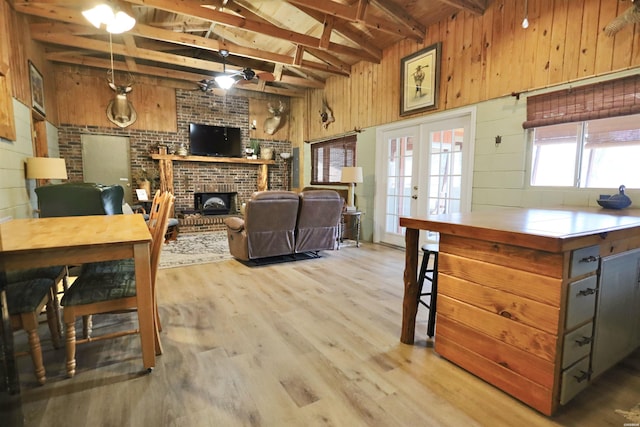 interior space with wooden walls, a fireplace, french doors, beam ceiling, and light wood finished floors