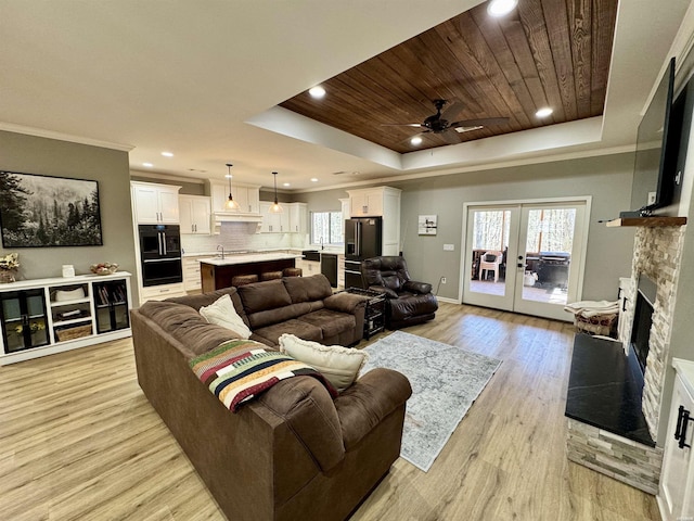 living room with crown molding, wood ceiling, light wood-style flooring, a fireplace, and a raised ceiling