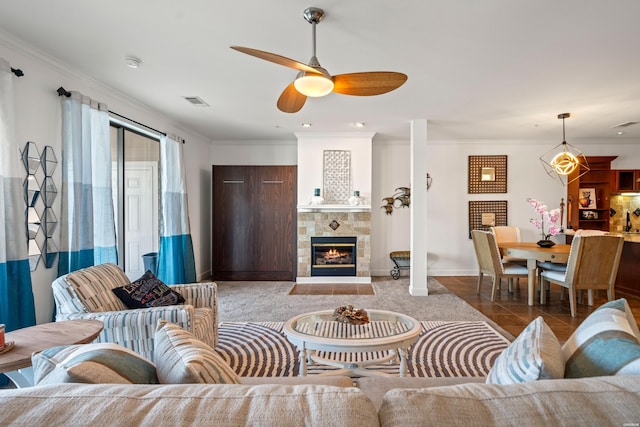 living room with crown molding, visible vents, a tiled fireplace, a ceiling fan, and dark tile patterned floors