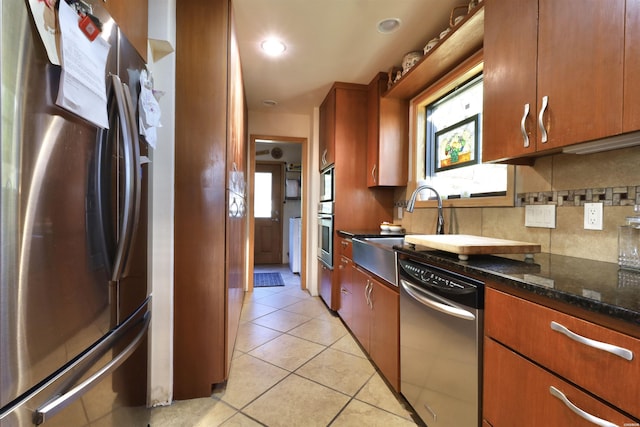 kitchen with light tile patterned floors, appliances with stainless steel finishes, a wealth of natural light, decorative backsplash, and dark stone countertops