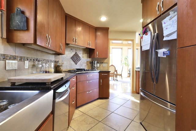 kitchen featuring tasteful backsplash, dark countertops, appliances with stainless steel finishes, brown cabinets, and light tile patterned flooring