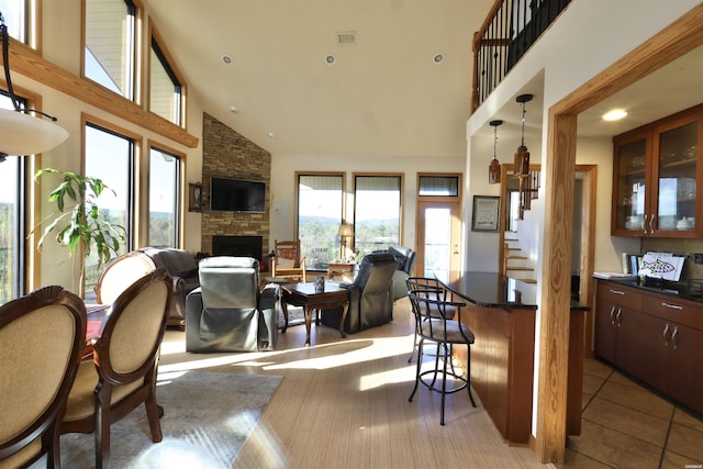 interior space featuring high vaulted ceiling, a stone fireplace, open floor plan, hanging light fixtures, and dark countertops