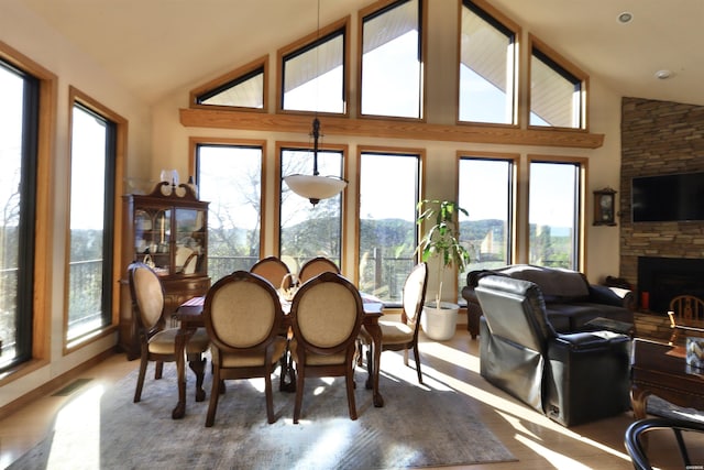 dining room with high vaulted ceiling, visible vents, wood finished floors, and a stone fireplace