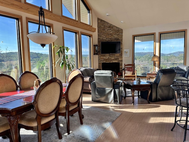 dining space with light wood-style floors, a fireplace, and high vaulted ceiling