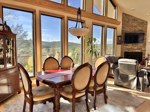 dining area with light wood-style floors, a fireplace, and high vaulted ceiling