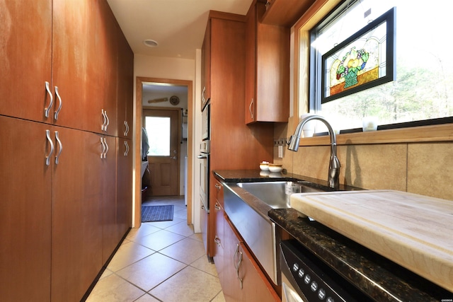 kitchen featuring light tile patterned floors, dishwasher, brown cabinets, dark stone countertops, and oven