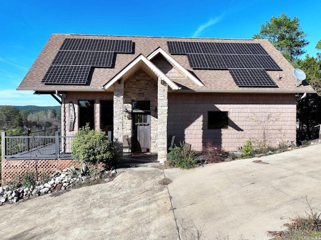 view of front facade featuring stone siding, roof mounted solar panels, and roof with shingles