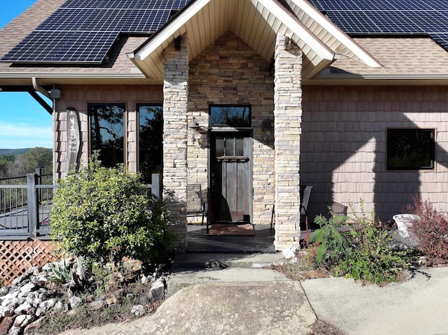 property entrance featuring solar panels, a shingled roof, and stone siding