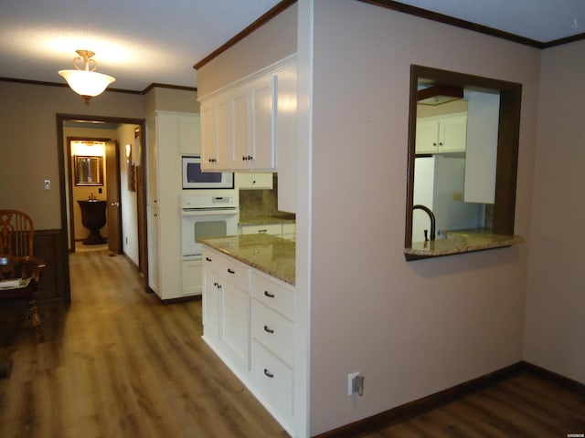 kitchen with white appliances, white cabinetry, ornamental molding, light stone countertops, and dark wood finished floors