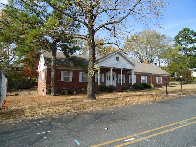 greek revival house with covered porch, a chimney, fence, and brick siding